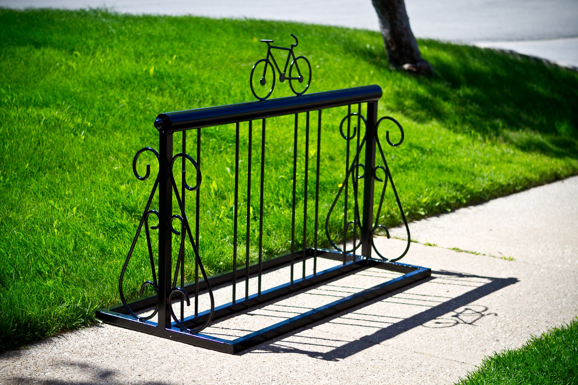 Decorative commercial bike rack installed beside a park pathway, providing secure outdoor bicycle parking for public spaces and businesses.