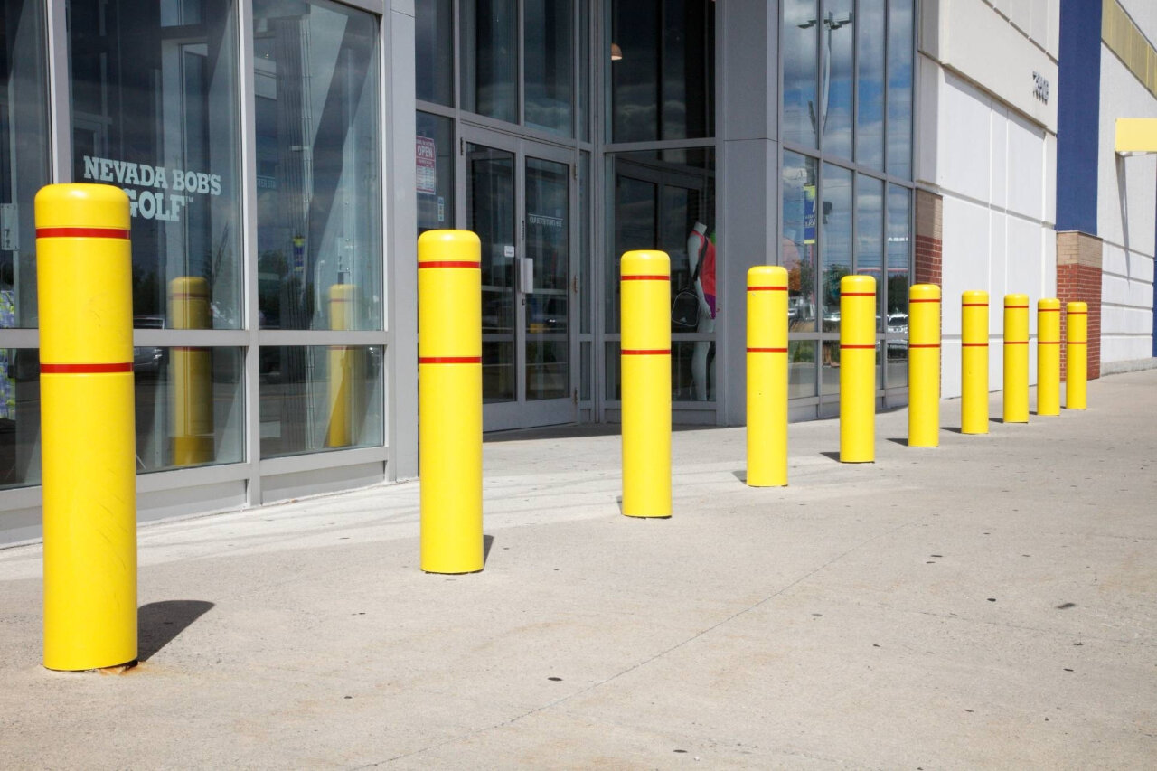 Yellow safety bollards installed outside retail store entrance in commercial shopping plaza.