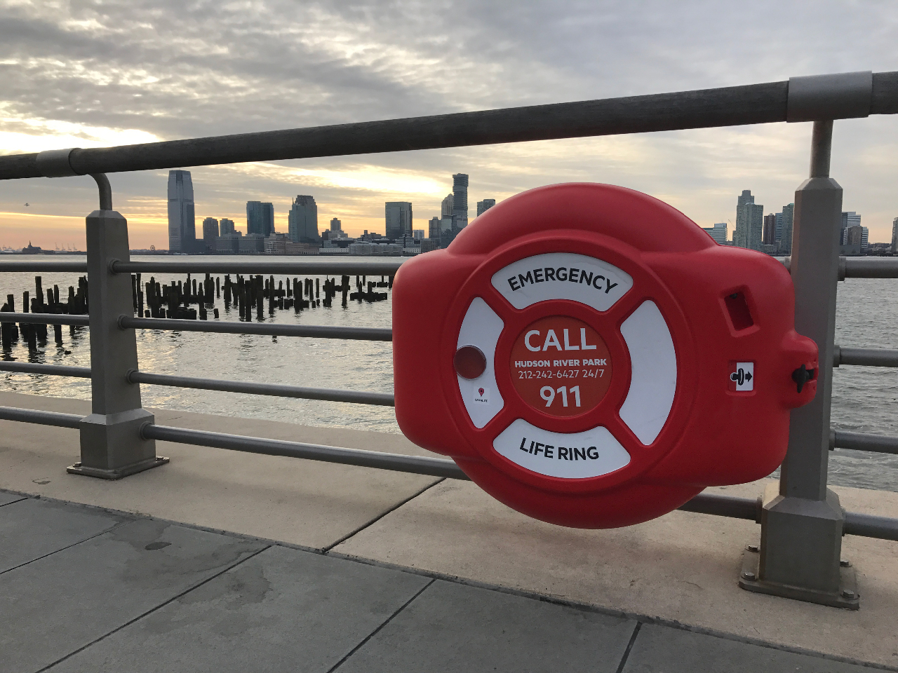 Commercial lifebuoy ring housing installed on waterfront railing, secure emergency water safety equipment for municipal and public access shoreline areas.